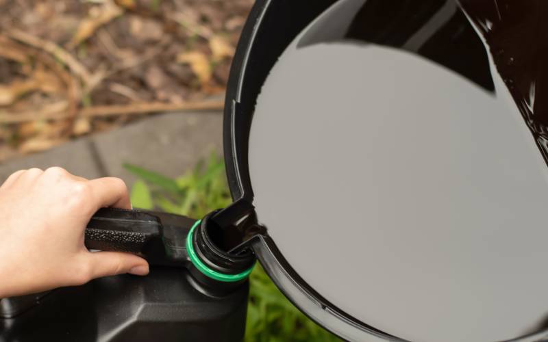 A person is steadily holding a plastic jug. They are pouring oil from a large pan directly into a container.