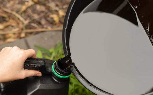 A person is steadily holding a plastic jug. They are pouring oil from a large pan directly into a container.