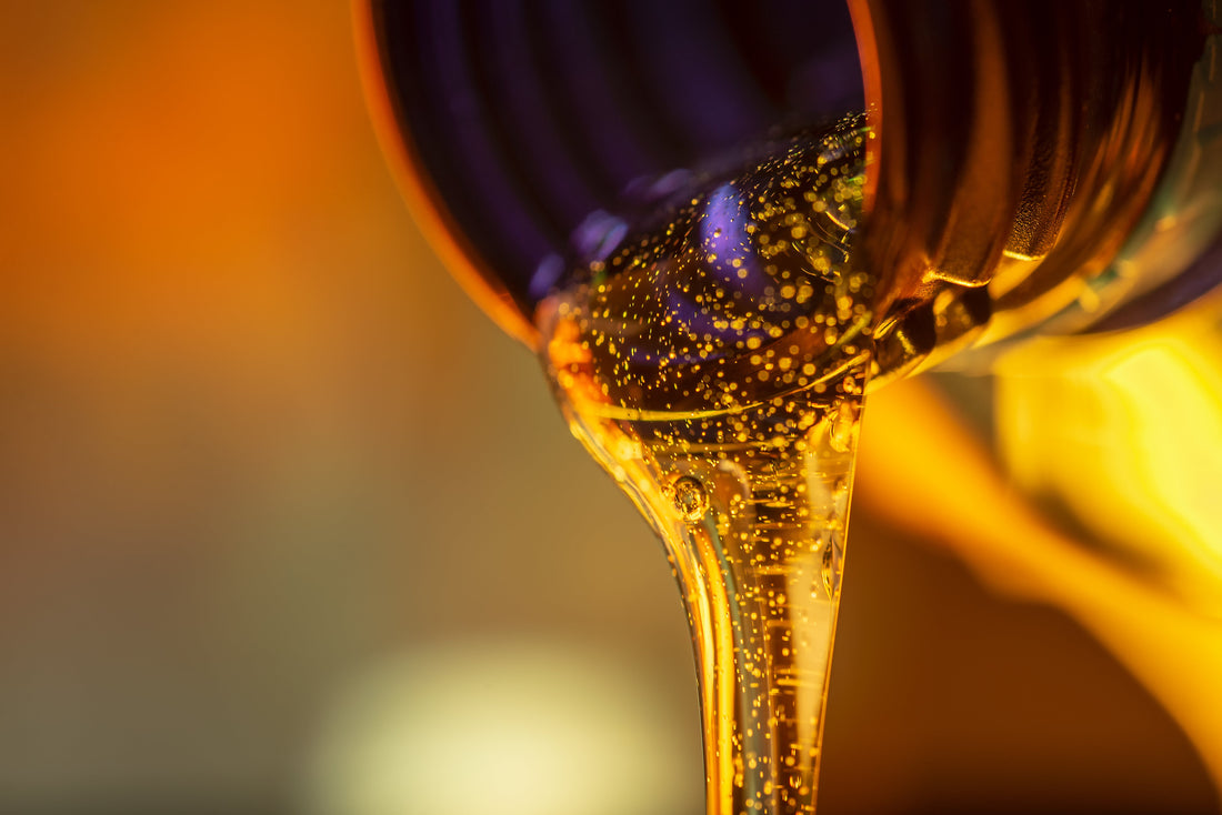 Closeup view of thick golden engine oil pouring from the mouth of a bottle. Several visible bubbles are in the oil itself.