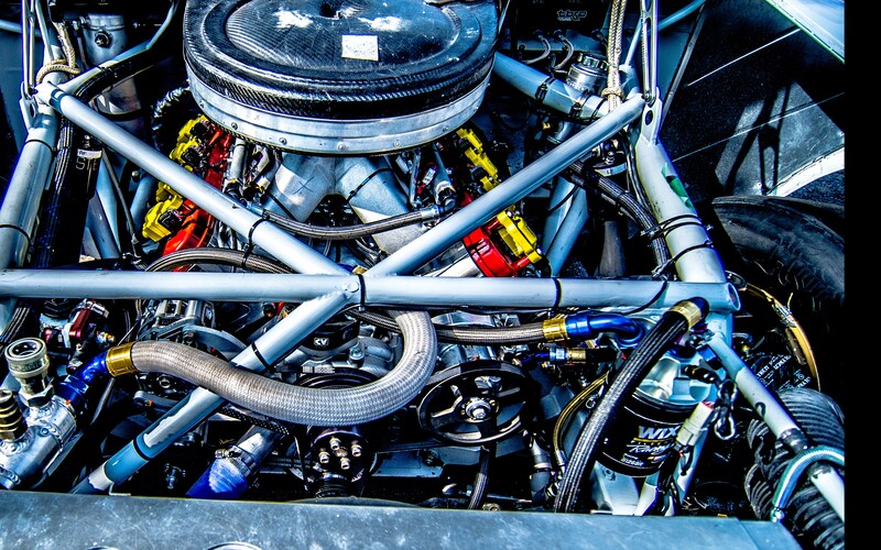 A well-maintained race car engine block. Several large cables and bright red or yellow parts are inside.