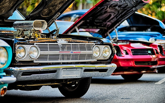 A row of vintage cars with their hoods up. Many of the vehicles feature modified engine blocks and unique features.