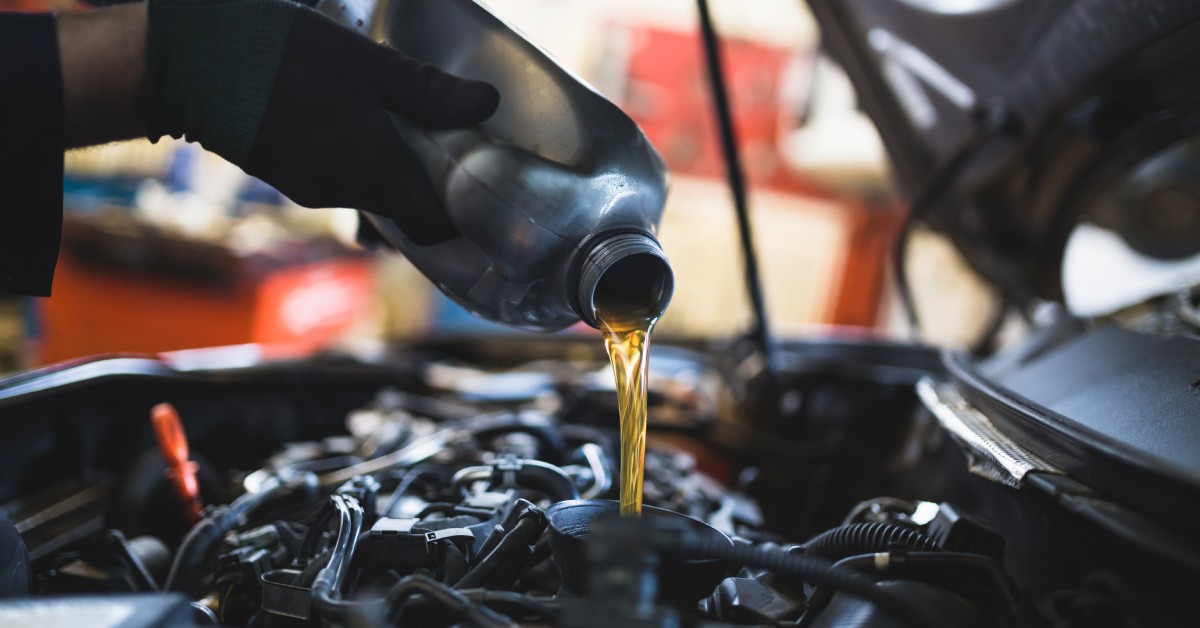 A mechanic working inside an autobody shop slowly pours oil into a car’s engine, enhancing its safety and longevity.