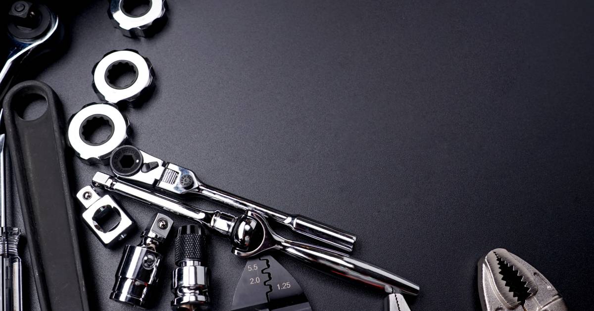 A set of tools and bolts for an engine lay against a dark grey background. The tools are all shiny and metal.