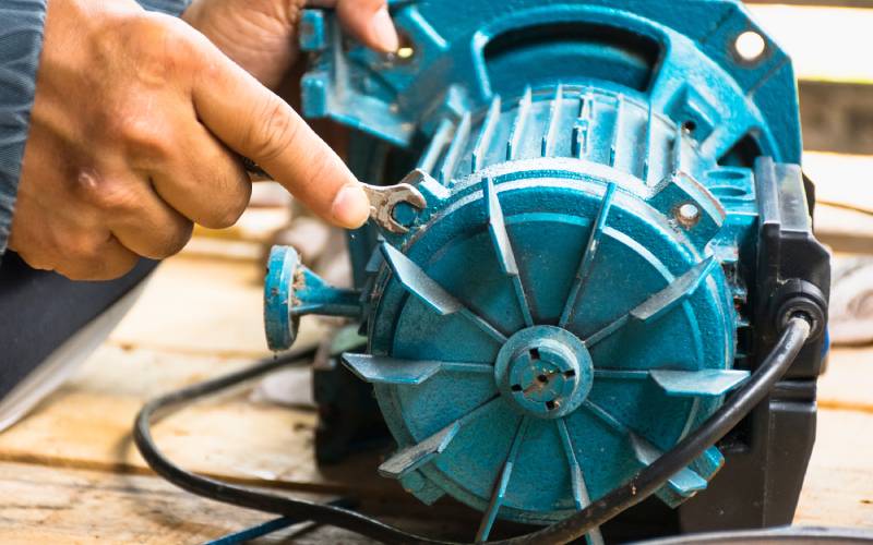 A person works on a blue rotor oil pump for a car. The top of the oil pump exposes red and yellow wires.