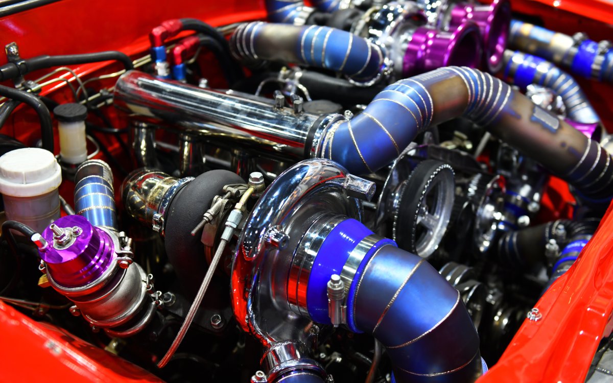 A close-up of a car's turbo engine components. Light reflects off of the turbo engine in a colorful array.