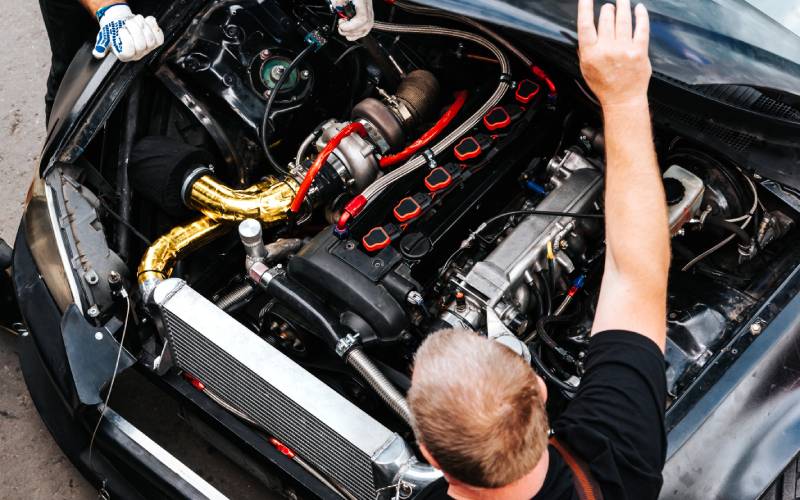 Two men looking under the hood of a race car. One is holding up the hood as they examine the engine.