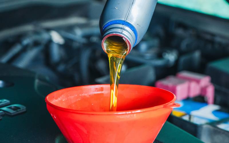 Closeup of oil being poured into a vehicle engine. The oil is spilling into a wide-mouthed red funnel.