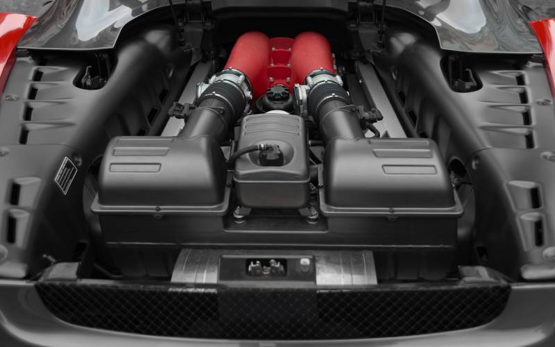 A shiny chrome engine sits in the back block of a vehicle. The hood is lifting up to reveal the engine.