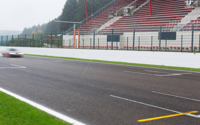 A blurry race car speeding through an empty, foggy racetrack. The bleachers in the background are also empty.