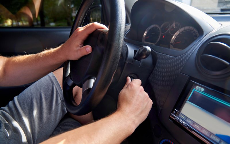 Man sitting in driver's seat of car and trying to turn the key. None of the dials on the dashboard are activated.