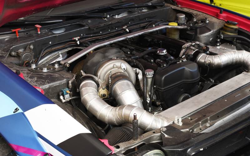 A close-up of the internal components of a vehicle's engine. A large silver pipe snakes along the front side of it.