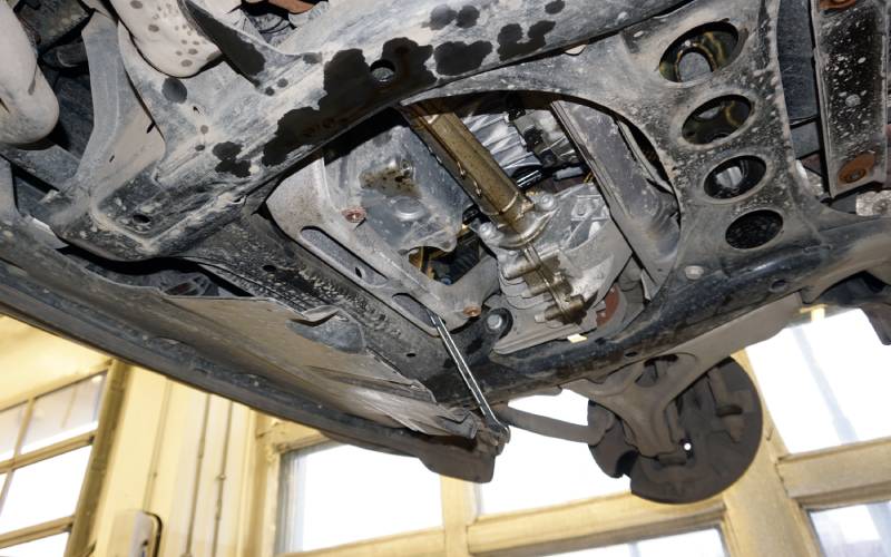 Underside of a lifted car at a mechanic's shop. There are several visible oil stains on the vehicle's undercarriage.