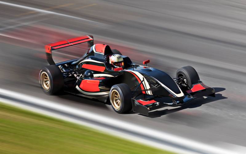 A person is driving a Formula 1 racing car along a track. They're moving so fast that there's slight motion blur.