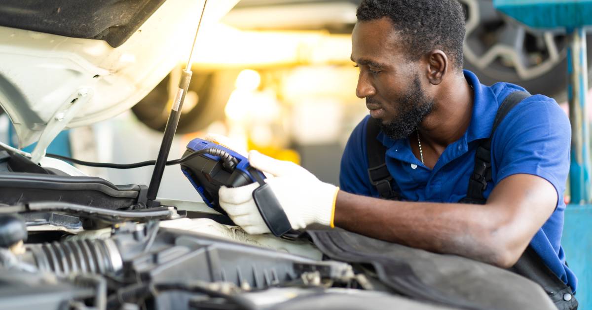 A professional male auto mechanic is inspecting a car’s engine with diagnostic testing software.