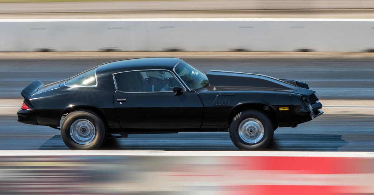 A classic drag race car speeds down a strip, engine roaring as it descends the track to beat its competitor.